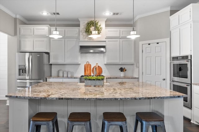 kitchen with hanging light fixtures, appliances with stainless steel finishes, a kitchen island with sink, and white cabinets