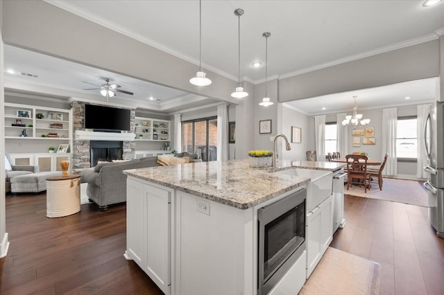 kitchen featuring pendant lighting, appliances with stainless steel finishes, a kitchen island with sink, light stone counters, and white cabinets