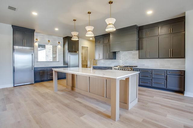 kitchen featuring pendant lighting, sink, appliances with stainless steel finishes, custom range hood, and an island with sink