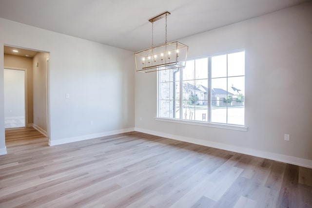 unfurnished room featuring a chandelier and light wood-type flooring