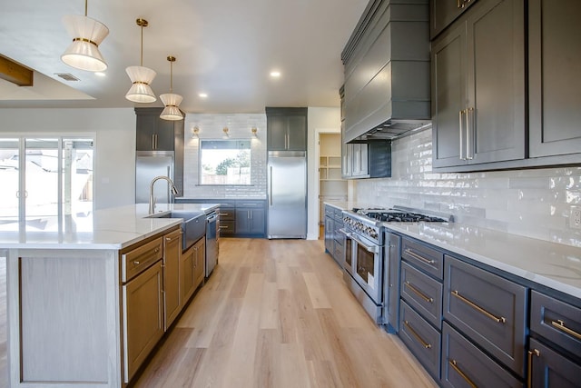 kitchen featuring sink, high quality appliances, custom range hood, pendant lighting, and light stone countertops