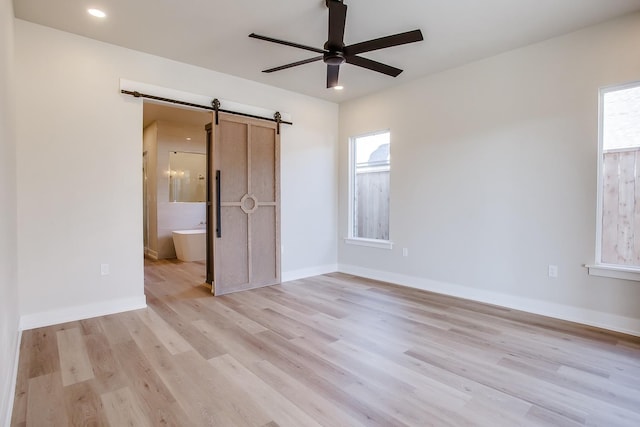 unfurnished bedroom with multiple windows, a barn door, light hardwood / wood-style floors, and ensuite bath