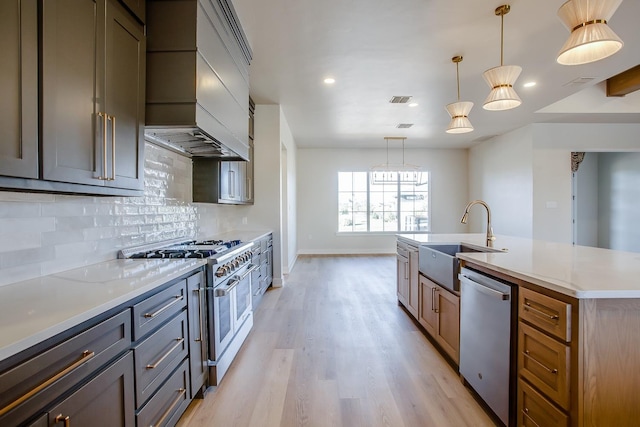 kitchen with pendant lighting, sink, stainless steel appliances, tasteful backsplash, and a center island with sink