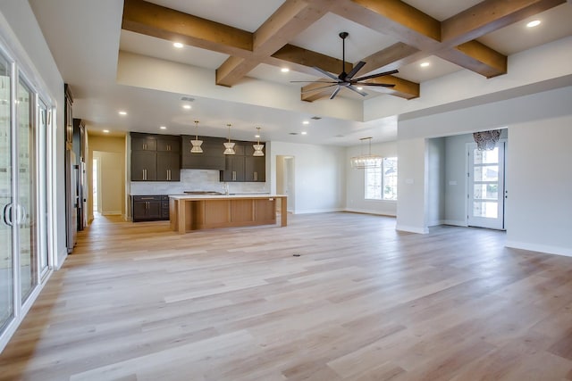 interior space with ceiling fan with notable chandelier, decorative backsplash, coffered ceiling, a kitchen island with sink, and light hardwood / wood-style flooring