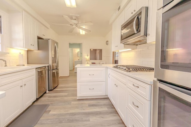 kitchen featuring sink, light wood-type flooring, appliances with stainless steel finishes, kitchen peninsula, and white cabinets