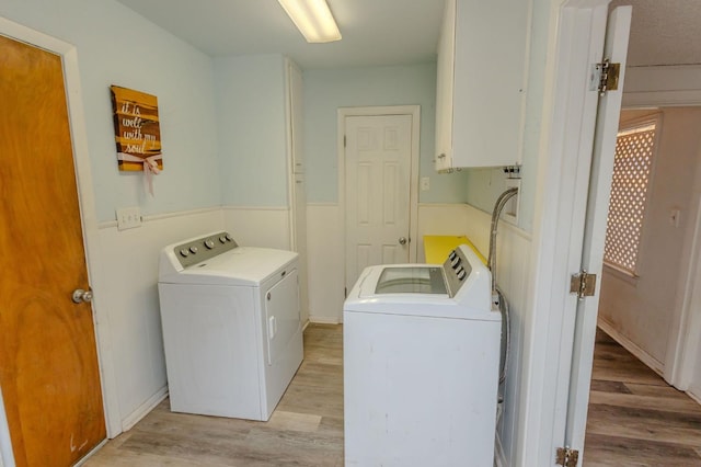 clothes washing area with cabinets, washing machine and dryer, and light hardwood / wood-style floors