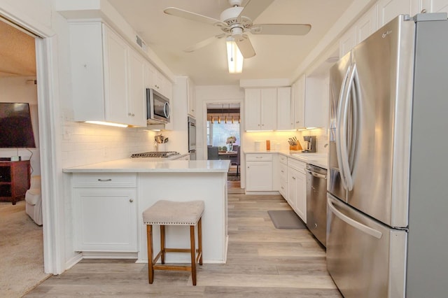 kitchen featuring a breakfast bar, stainless steel appliances, white cabinets, kitchen peninsula, and light wood-type flooring