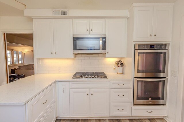 kitchen featuring white cabinetry, decorative backsplash, kitchen peninsula, and appliances with stainless steel finishes