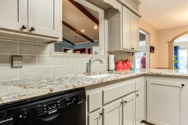 kitchen featuring sink, white cabinetry, light stone counters, black dishwasher, and backsplash