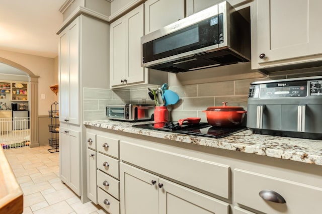 kitchen with light stone counters, white cabinetry, and backsplash