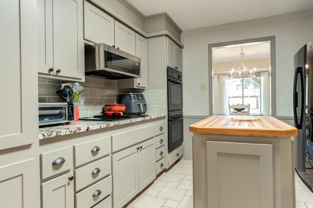 kitchen featuring wood counters, tasteful backsplash, a center island, a notable chandelier, and black appliances