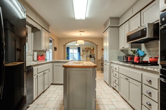 kitchen with a kitchen island, butcher block countertops, decorative light fixtures, backsplash, and black appliances