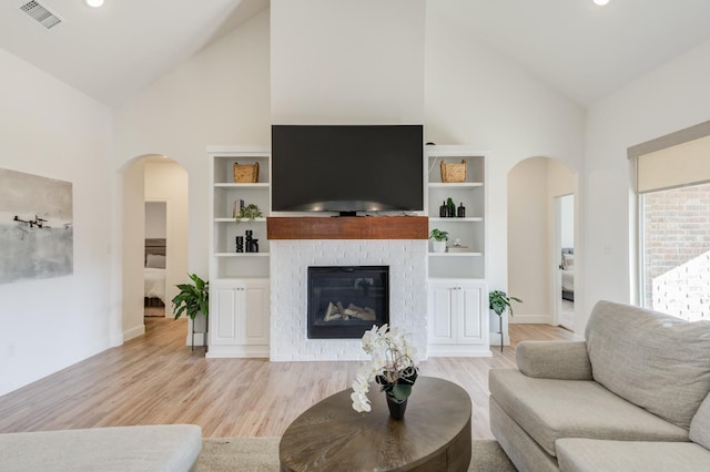 living room with a brick fireplace, light wood-type flooring, and high vaulted ceiling