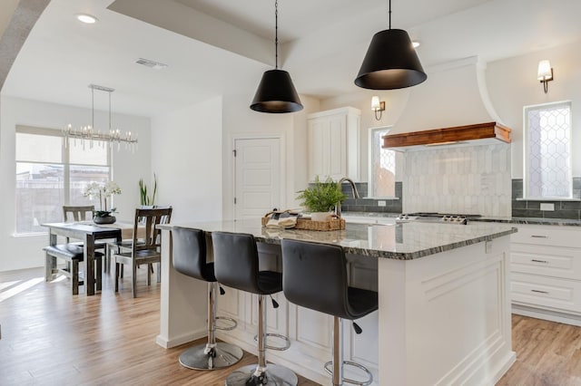 kitchen featuring light hardwood / wood-style floors, white cabinets, a kitchen island, decorative backsplash, and dark stone counters