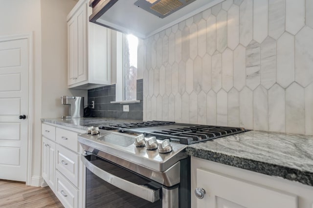 kitchen with white cabinetry, stainless steel gas stove, tasteful backsplash, and dark stone counters