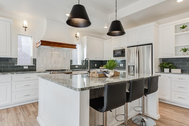 kitchen with a kitchen island with sink, light stone counters, custom range hood, white cabinets, and stainless steel fridge with ice dispenser