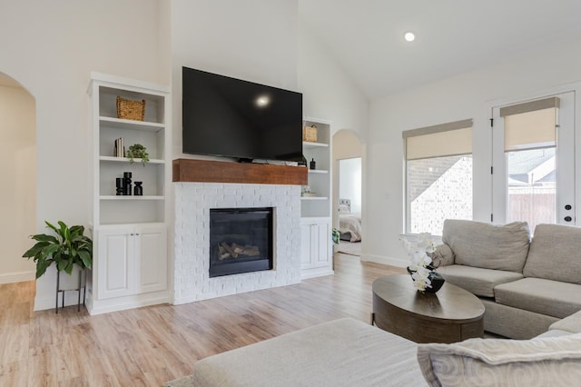 living room with high vaulted ceiling, built in features, a fireplace, and light hardwood / wood-style flooring