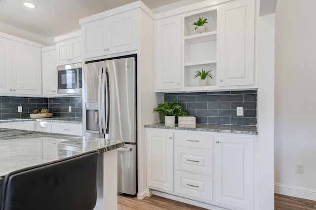 kitchen with white cabinetry, tasteful backsplash, light stone counters, appliances with stainless steel finishes, and light hardwood / wood-style floors