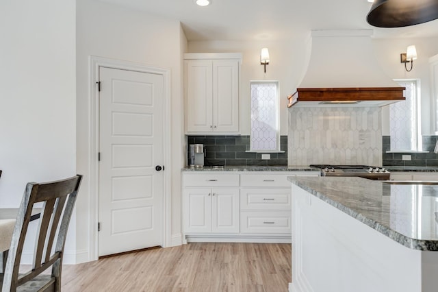 kitchen featuring custom exhaust hood, white cabinetry, light hardwood / wood-style floors, and decorative backsplash