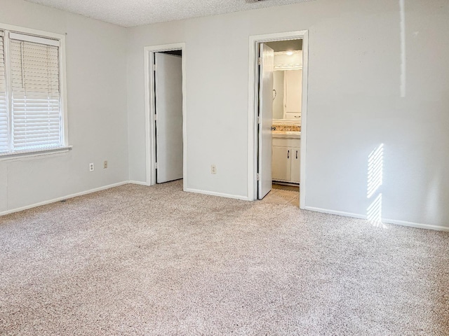 unfurnished bedroom featuring connected bathroom, light colored carpet, and a textured ceiling