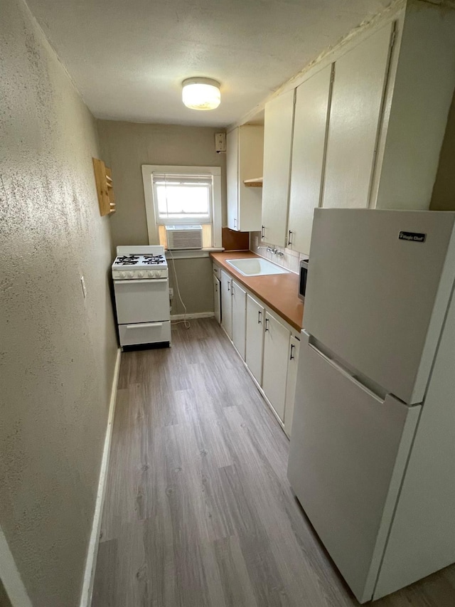 kitchen with sink, white cabinets, white appliances, a wall unit AC, and light hardwood / wood-style flooring