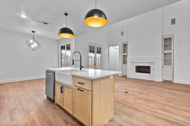 kitchen with built in features, sink, hanging light fixtures, a kitchen island with sink, and light brown cabinets