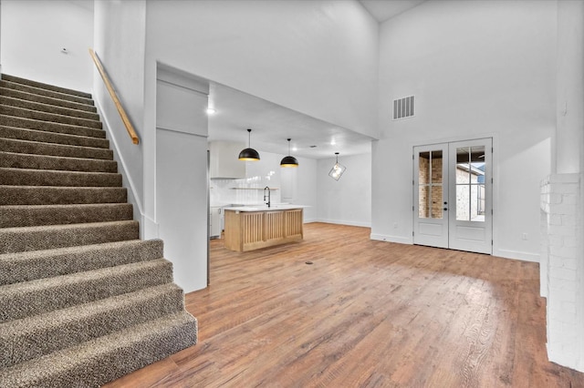 unfurnished living room with french doors, a towering ceiling, sink, and hardwood / wood-style flooring