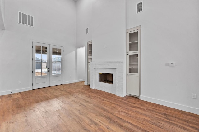 unfurnished living room with a brick fireplace, hardwood / wood-style floors, french doors, and a high ceiling