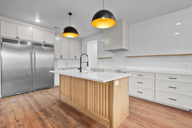 kitchen with pendant lighting, an island with sink, sink, white cabinets, and built in refrigerator