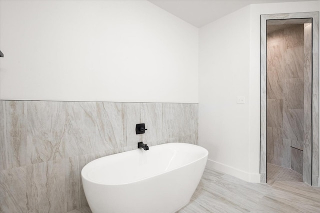 bathroom with a tub to relax in and tile walls