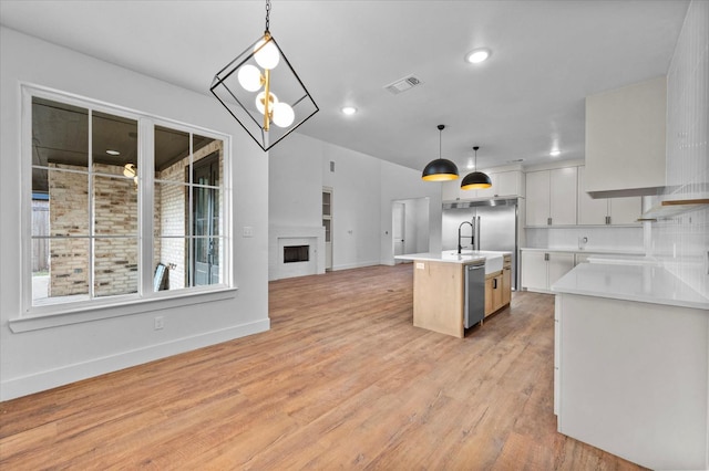 kitchen with sink, appliances with stainless steel finishes, white cabinetry, hanging light fixtures, and a center island with sink