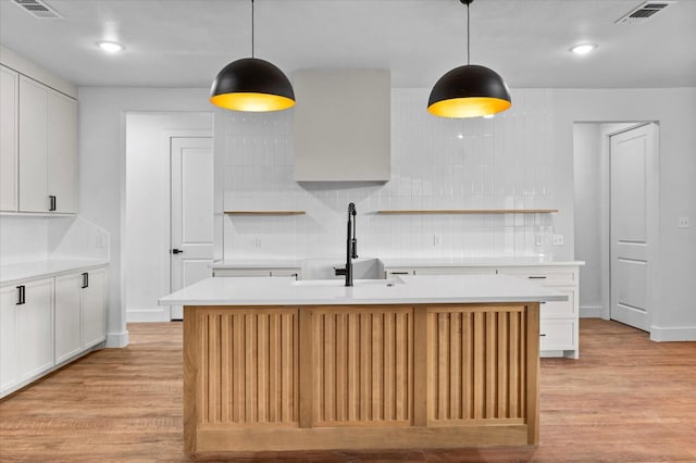 kitchen with tasteful backsplash, decorative light fixtures, an island with sink, and white cabinets