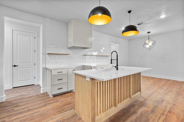 kitchen featuring a kitchen island with sink, backsplash, decorative light fixtures, and white cabinets