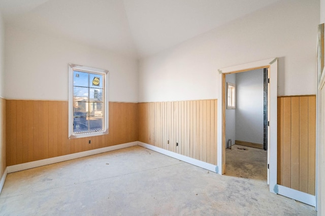 unfurnished room featuring plenty of natural light, vaulted ceiling, and wood walls