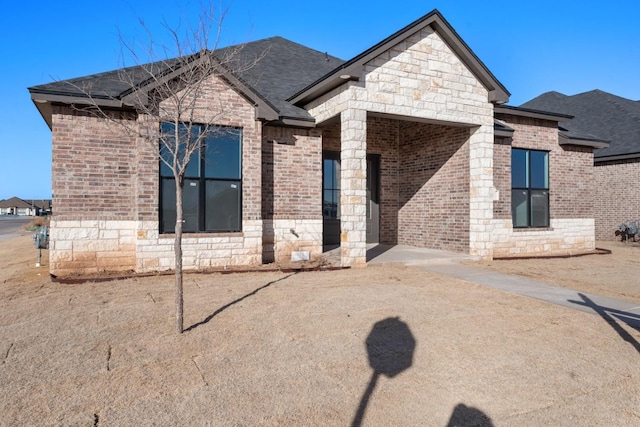 view of front facade with stone siding, a shingled roof, and brick siding