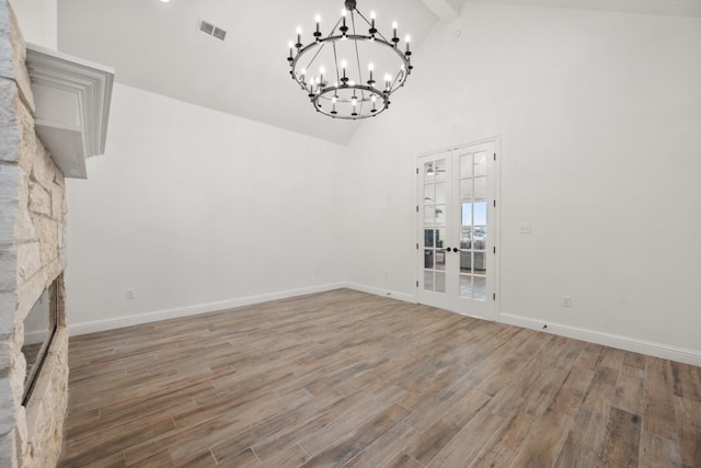 unfurnished living room with hardwood / wood-style flooring, high vaulted ceiling, a notable chandelier, a fireplace, and french doors