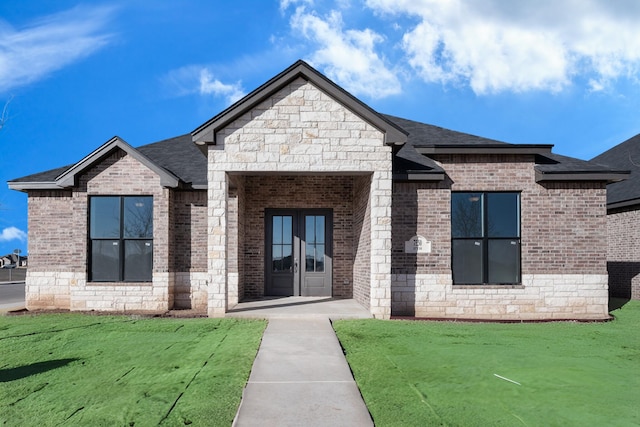 view of front of home featuring a front yard, french doors, brick siding, and roof with shingles