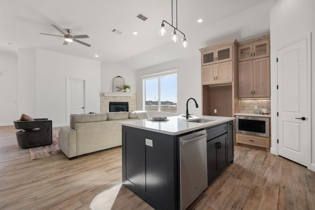 kitchen with dishwasher, a fireplace, light hardwood / wood-style floors, a center island with sink, and decorative light fixtures