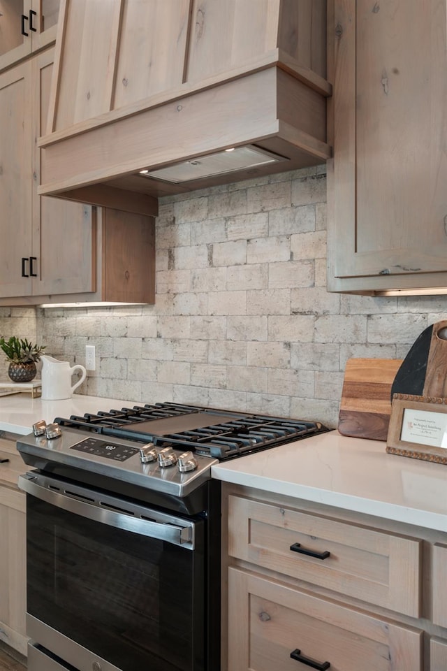 kitchen featuring tasteful backsplash, custom exhaust hood, stainless steel range with gas stovetop, and light brown cabinets