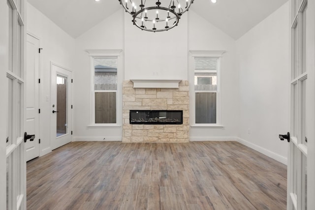 unfurnished living room with plenty of natural light, a notable chandelier, a fireplace, and light hardwood / wood-style floors