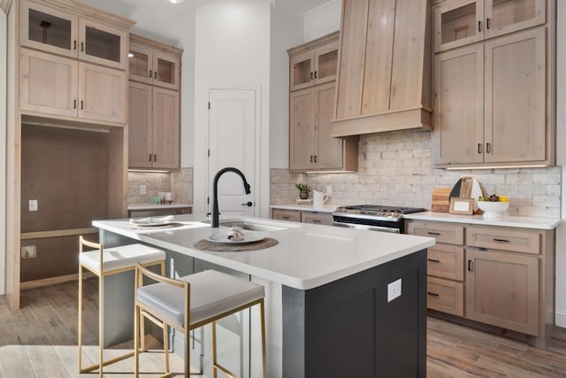 kitchen featuring sink, stainless steel gas stove, a kitchen breakfast bar, an island with sink, and light brown cabinets