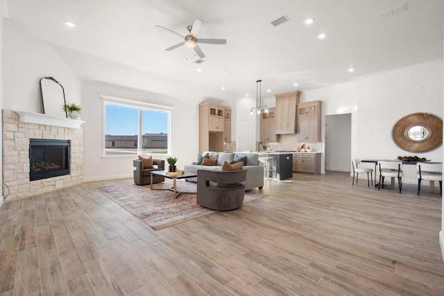 living room with sink, a stone fireplace, light hardwood / wood-style flooring, and ceiling fan