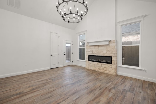 unfurnished living room featuring hardwood / wood-style flooring, a stone fireplace, a notable chandelier, and high vaulted ceiling