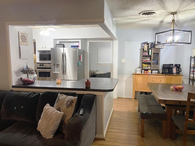 kitchen featuring a textured ceiling, hanging light fixtures, light wood-type flooring, stainless steel appliances, and ceiling fan with notable chandelier