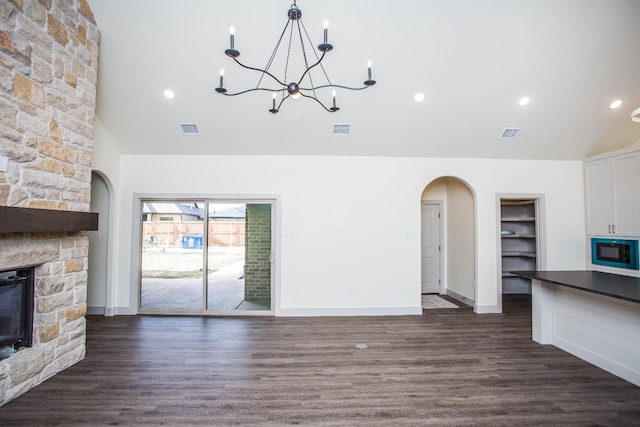 unfurnished living room featuring built in features, a stone fireplace, dark hardwood / wood-style floors, and lofted ceiling