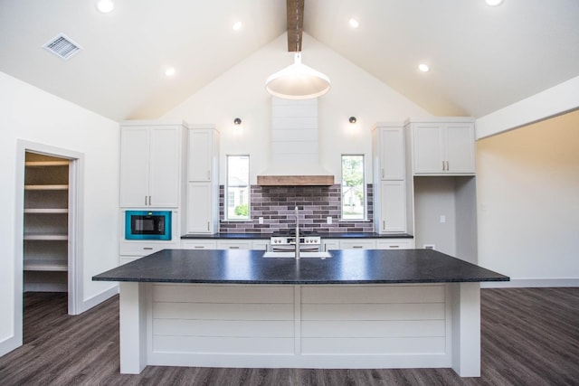 kitchen featuring white cabinetry, custom range hood, black microwave, and a center island with sink