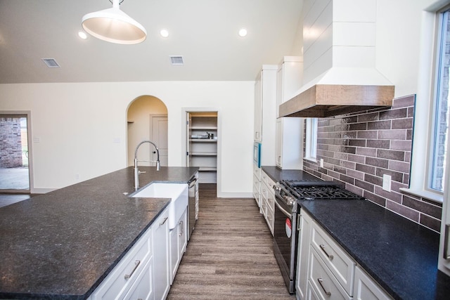 kitchen with custom exhaust hood, white cabinets, stainless steel gas range, and decorative light fixtures