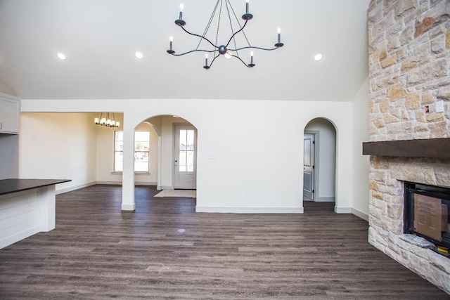 unfurnished living room with a stone fireplace, dark hardwood / wood-style floors, high vaulted ceiling, and a chandelier