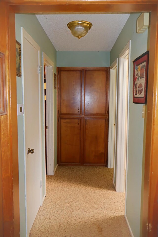 hall with light colored carpet and a textured ceiling