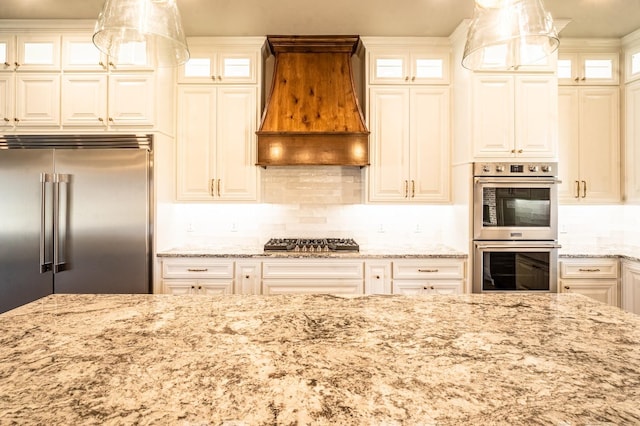 kitchen featuring premium range hood, decorative light fixtures, decorative backsplash, light stone counters, and stainless steel appliances